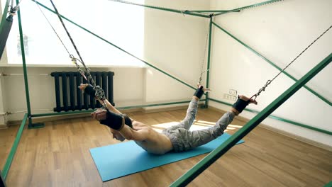 Young-man-doing-exircise-on-quartering-yoga-equipment-and-pull-his-arms-and-legs-with-ropes