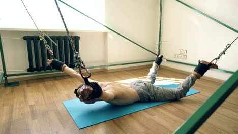Junger-Mann-tun-Exircise-auf-Kasernierung-Yoga-Ausrüstung-und-ziehen-Sie-seine-Arme-und-Beine-mit-Seilen