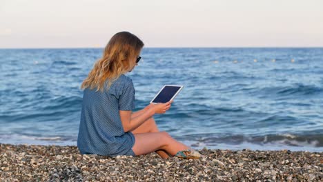 blonde-Frau,-Tablette,-am-Strand-am-Abend-Zeit,-weiche-Sonnenlicht-e-Buch-zu-lesen