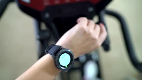 PoV-of-woman-doing-cardio-on-elliptical-trainer-checking-workout-on-smart-watch