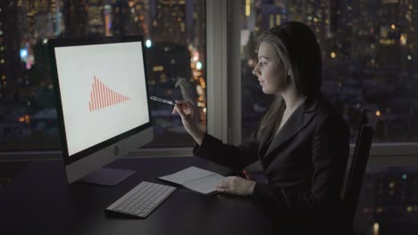 Good-Looking-Woman-Working-with-a-Computer,-Ballpoint-Pen,-Pad-and-a-Phone-in-Multistory-Office-Building.-Calling-Colleagues,-Big-City-Can-Be-Seen-through-Window.