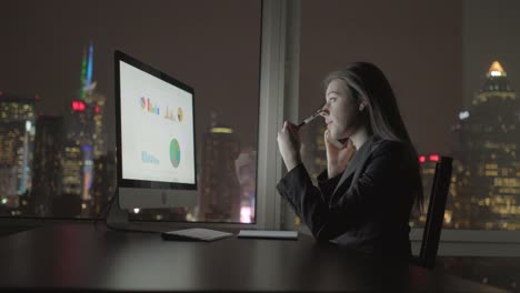 Atractiva-morena-trabajando-en-la-tabla-de-la-oficina-por-la-noche.-Empresaria-de-trabajo-con-ordenador-y-teléfono-inteligente-oficina-con-vista-al-paisaje-urbano.