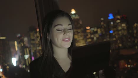 Attractive-Brunette-Working-in-Office-at-Night.-Businesswoman-Working-with-Digital-Tablet-in-Office-with-Cityscape-View.