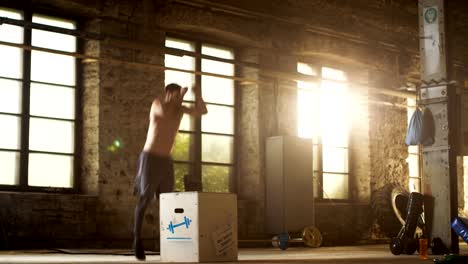 Athletic-Shirtless-Fit-Man-Energetically-Box-Jumps-in-Hardcore-Gym-doing-Part-of-Cross-Fitness-Training-Program.-Man-is-Sweaty-from-Intense-Workout/-Exercise,-Gym-is-in-Industrial-Factory-Location.