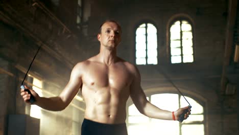 Athletic-Shirtless-Fit-Man-Exercises-with-Jump-/-Skipping-Rope-in-a-Deserted-Factory-Hardcore-Gym.-He's-Covered-in-Sweat-from-His-Intense-Fitness-Training.