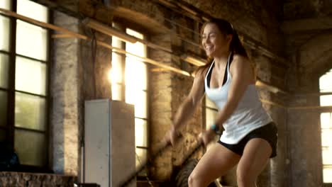 Mujer-atlética-en-un-gimnasio-de-ejercicios-con-cuerdas-de-batalla-durante-su-entrenamiento-de-Cross-Fitness-/-entrenamiento-de-intervalo-de-alta-intensidad.-Ella-es-Muscular-y-sudoroso,-gimnasio-en-Nave-Industrial.