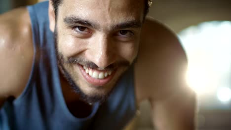 Exhausted-Bend-Muscular-Man-Looks-into-Camera-and--Rests-After-Intensive-Workout.-He's-In-a-Gym-and-Covered-in-Sweat.-He-Tries-to-Catch-a-Breath.