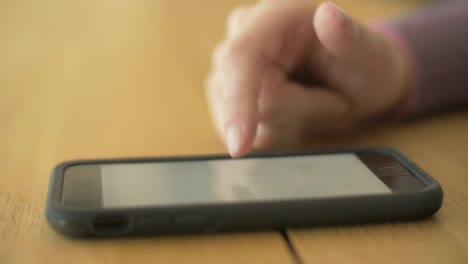 Closeup-Of-Woman's-Finger-Scrolling-Screen-On-Smartphone-At-Table