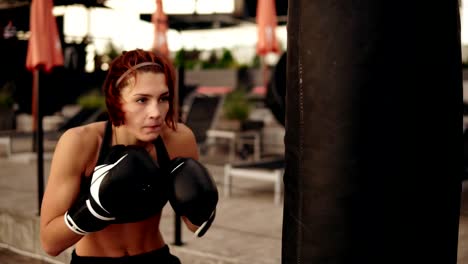 Junge-sportliche-Boxerin-in-Handschuhen-treten-ein-Boxsack-mit-ihren-Händen-und-Ellenbogen.-Training-außerhalb.-Boxerin-Boxhandschuhe-training.-Schuss-in-4k