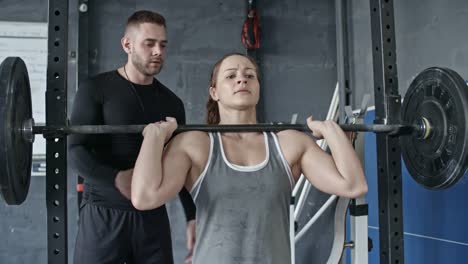 Personal-Trainer-Supporting-Woman-while-Doing-Barbell-Front-Squat