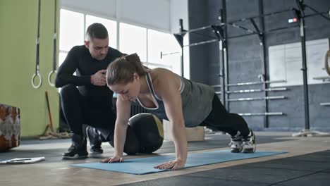 Cross-Training-Instructor-unterstützt-Frau-während-sie-Doing-Push-ups