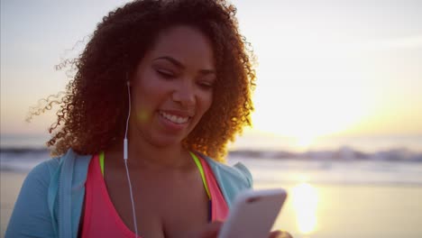 Ethnic-female-in-sportswear-using-phone-on-beach