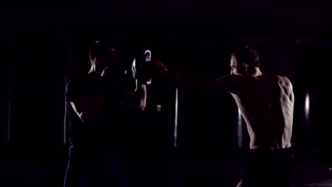 Boxer-man-hits-punching-bag-with-his-fists.-Trainer-Holds.-Boxer-hits-punching-bag-that-her-partner.Part-of-his-gym-training.-Fighter-training-with-punching-bag