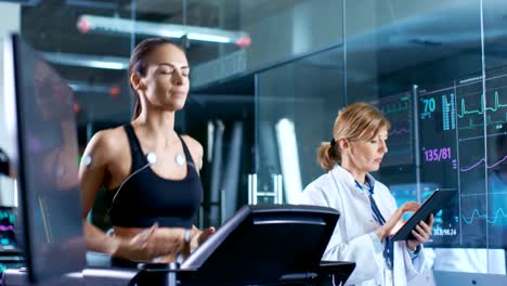 Beautiful-Woman-Athlete-Runs-on-a-Treadmill-with-Electrodes-Attached-to-Her-Body,-Female-Physician-Uses-Tablet-Computer-and-Controls-EKG-Data-Showing-on-Laboratory-Monitors.