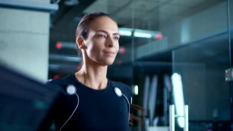 Beautiful-Woman-Athlete-Walks-on-a-Treadmill-with-Electrodes-Attached-to-Her-Body,-while-Scientist-Supervises-Her-EKG-Data-Showing-on-Laboratory-Monitors.