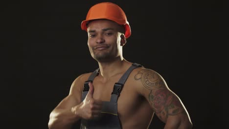 Happy-muscular-African-male-builder-in-hardhat-smiling-showing-thumbs-up