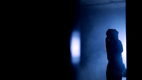 Closeup-view-of-a-young-woman-having-a-break-after-a-tough-training-on-a-boxing-bag.-Silhouettes-of-a-female-boxer-trains-in-a-dark-gym-with-punching-bag