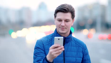 A-young-attractive-man-uses-a-mobile-phone-in-a-night-city.