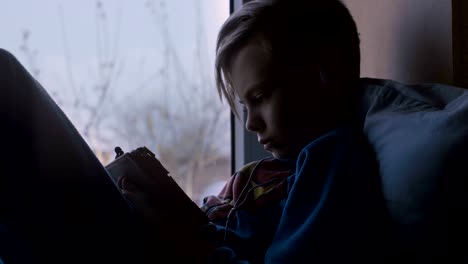 Kid-using-tablet-on-window-sill