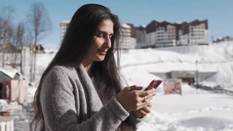 Señora-morena-adulta-está-contestando-en-mensaje-en-su-teléfono,-al-aire-libre-en-días-de-invierno