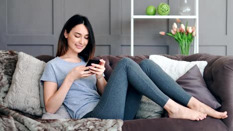 Young-pretty-woman-sitting-on-sofa-with-smartphone