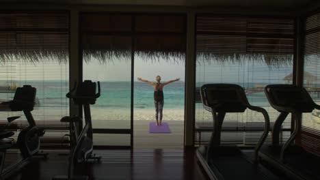 Rückansicht-Aufnahme-einer-Fit-junge-Frau-beim-Yoga-auf-einer-Veranda-ein-Fitness-Studio-Hütte.-Im-Hintergrund-exotische-Insel-mit-schönen-ruhigen-Meer-und-klaren-sonnigen-Himmel.