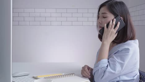 Hermosa-joven-sonriente-mujer-asiática-trabajando-en-ordenador-portátil-mientras-está-sentado-en-una-sala-de-estar-en-casa.-Mujer-de-negocios-asiática-con-teléfono-para-el-trabajo-en-su-oficina-en-casa.-Disfrutando-en-casa.