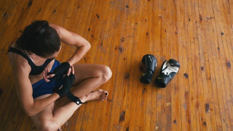 Beautiful-Kickboxing-mixed-race-woman-putting-on-punching-wraps-bandage-in-fitness-studio-fierce-strength-fit-body