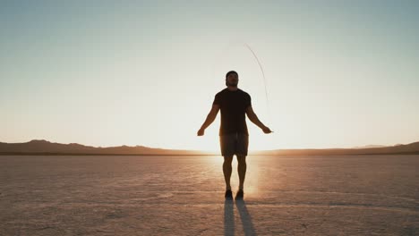 Hombre-atlético-lenta-trabajando-por-fuera-en-el-desierto-en-la-cuerda-de-salto-al-atardecer