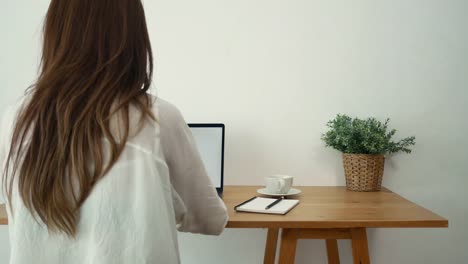 Beautiful-young-smiling-woman-working-on-laptop-while-enjoying-drinking-warm-coffee-sitting-in-a-living-room-at-home.-Enjoying-time-at-home.-Asian-business-woman-working-in-her-home-office.