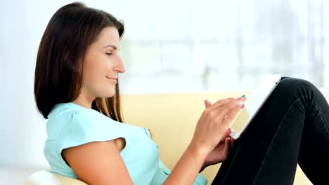 Young-woman-is-relaxing-on-comfortable-couch-and-using-digital-tablet-indoors