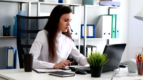 Frau-auf-Kopfhörer-sprechen-und-mit-Laptop-im-modernen-Büro