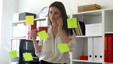 businesswoman-in-white-blouse-considering-sticky-notes-on-glass-and-talking-on-phone