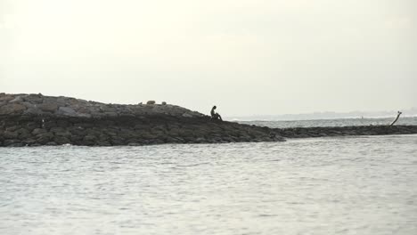 Pescador-sentado-en-dique-en-puesta-del-sol