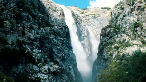 Huge-waterfall-in-the-mountains,-a-powerful-stream-of-water-falls-from-the-cliff,-slow-motion