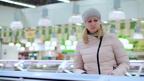 A-woman-in-winter-clothes-walks-around-the-supermarket.-Chooses-products-in-the-refrigerator-in-the-store