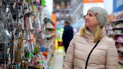 A-woman-in-a-hat-and-a-down-jacket-walks-through-the-supermarket.-She-looks-at-the-goods-on-the-shelves,-chooses-a-purchase.