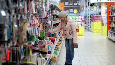 A-woman-in-a-hat-and-a-down-jacket-walks-through-the-supermarket.-She-takes-the-goods-from-the-shelf,-chooses-a-purchase.