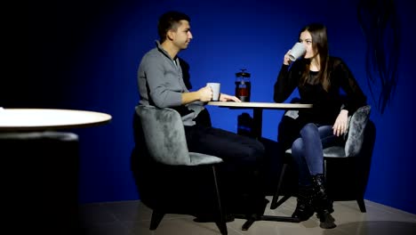 Beautiful-man-and-woman-sitting-in-the-cafe-at-the-table-during-coffee-break.-They-are-talking-and-drinking-hot-tea.