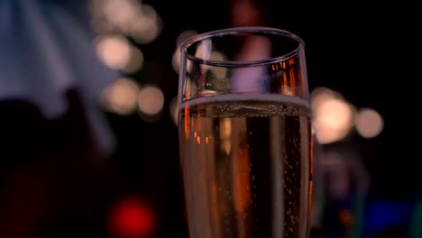 Glass-of-sparkling-champagne,-dancing-people-in-the-background,-party,-bokeh