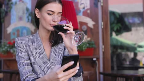 Mujer-sonriente-bebiendo-vino-y-usar-el-teléfono-en-el-restaurante