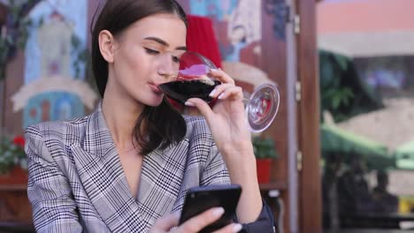 Mujer-sonriente-bebiendo-vino-y-usar-el-teléfono-en-el-restaurante