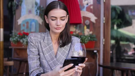 Lächelnde-Frau-trinken-Wein-und-mit-Telefon-im-Restaurant