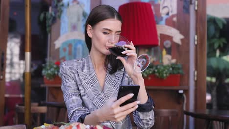 Smiling-Woman-Drinking-Wine-And-Using-Phone-At-Restaurant