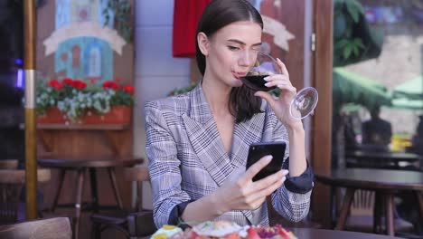 Mujer-sonriente-bebiendo-vino-y-usar-el-teléfono-en-el-restaurante