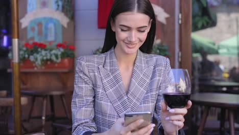 Mujer-sonriente-bebiendo-vino-y-usar-el-teléfono-en-el-restaurante