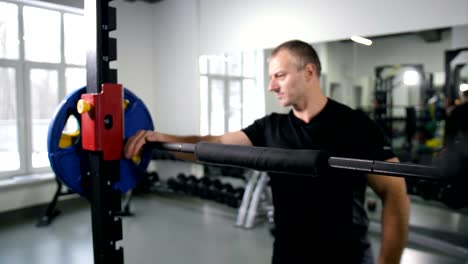 A-strong-man-fits-the-barbell,-takes-it-on-the-shoulders-and-does-squats-4K-Slow-Mo