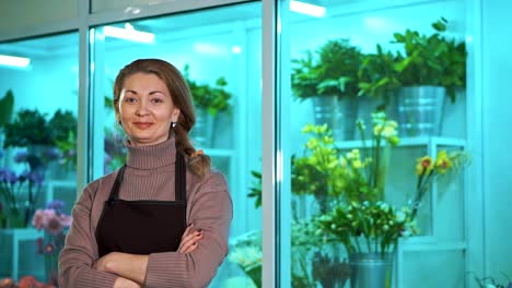 Frau-Florist-schaut-die-Kamera-auf-dem-Hintergrund-der-Schaufenster-von-Blumen.