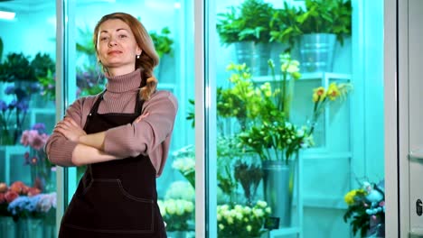 Frau-Florist-schaut-die-Kamera-auf-dem-Hintergrund-der-Schaufenster-von-Blumen.