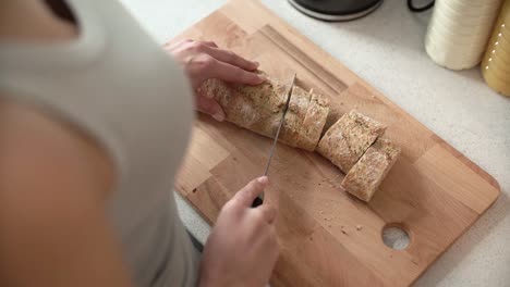 Cutting-Bread-On-Wooden-Board-By-Woman-Hands-Closeup